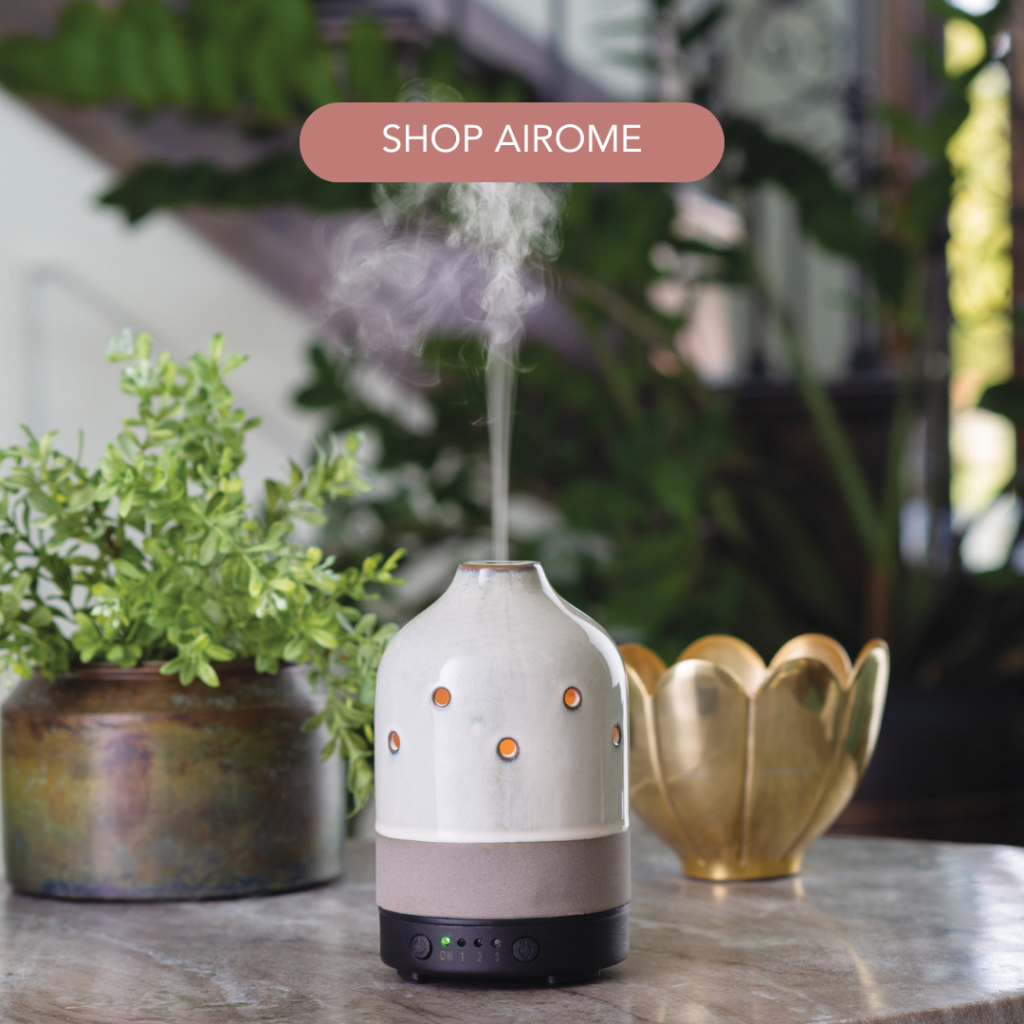 'Shop Airome' button over a white ceramic essential oil diffuser releasing mist beside plants