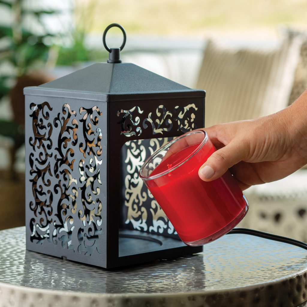 Hand placing a red candle into a black filigree metal lantern candle warmer